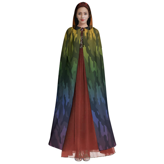 A woman modeling a long hooded cape with a multicolor camouflage-like gradient pattern in green, yellow, blue, and purple, worn over a rust-red dress against a plain white background.